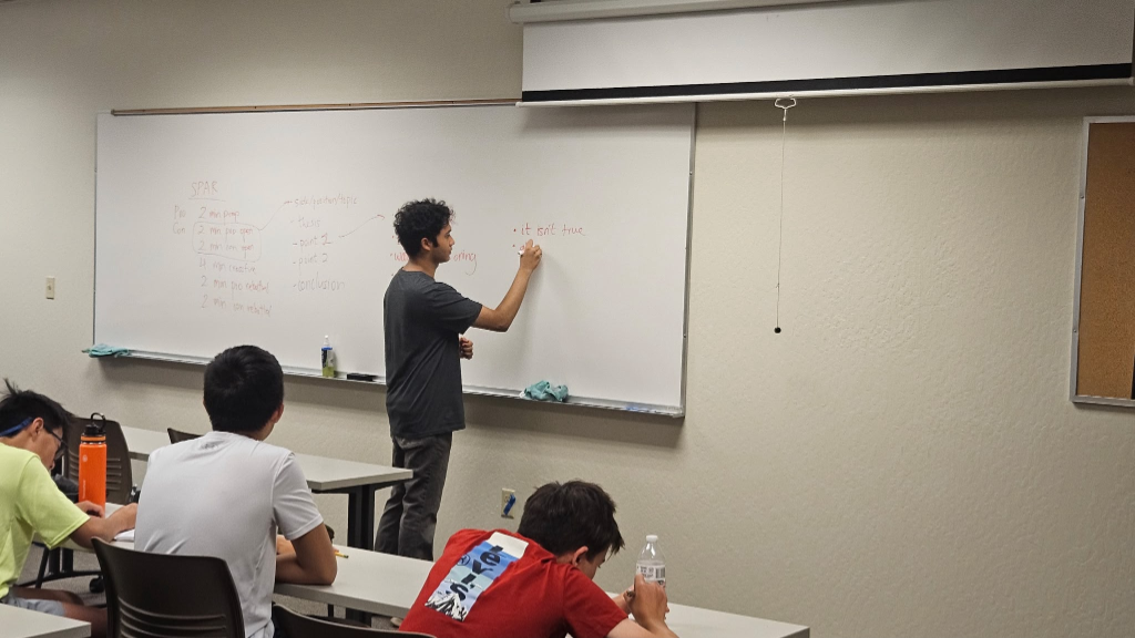 Instructor explaining SPAR debate structure on whiteboard at 2026 camp